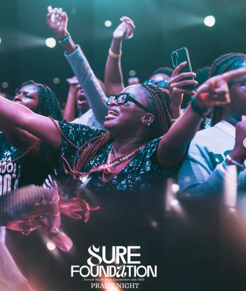 Delegates at praise night with hands raised under stage lights